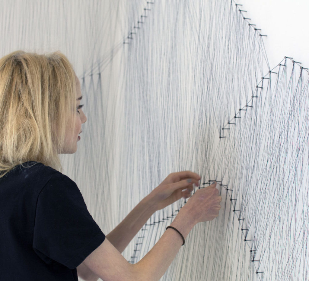 Amelia repeatedly weaves and knots embroidery thread multiple times around nails hammered into the wall. The overall affect (or effect I can never work out which one I need to use) creates a delicate mountain structure that rises 3 metres high.