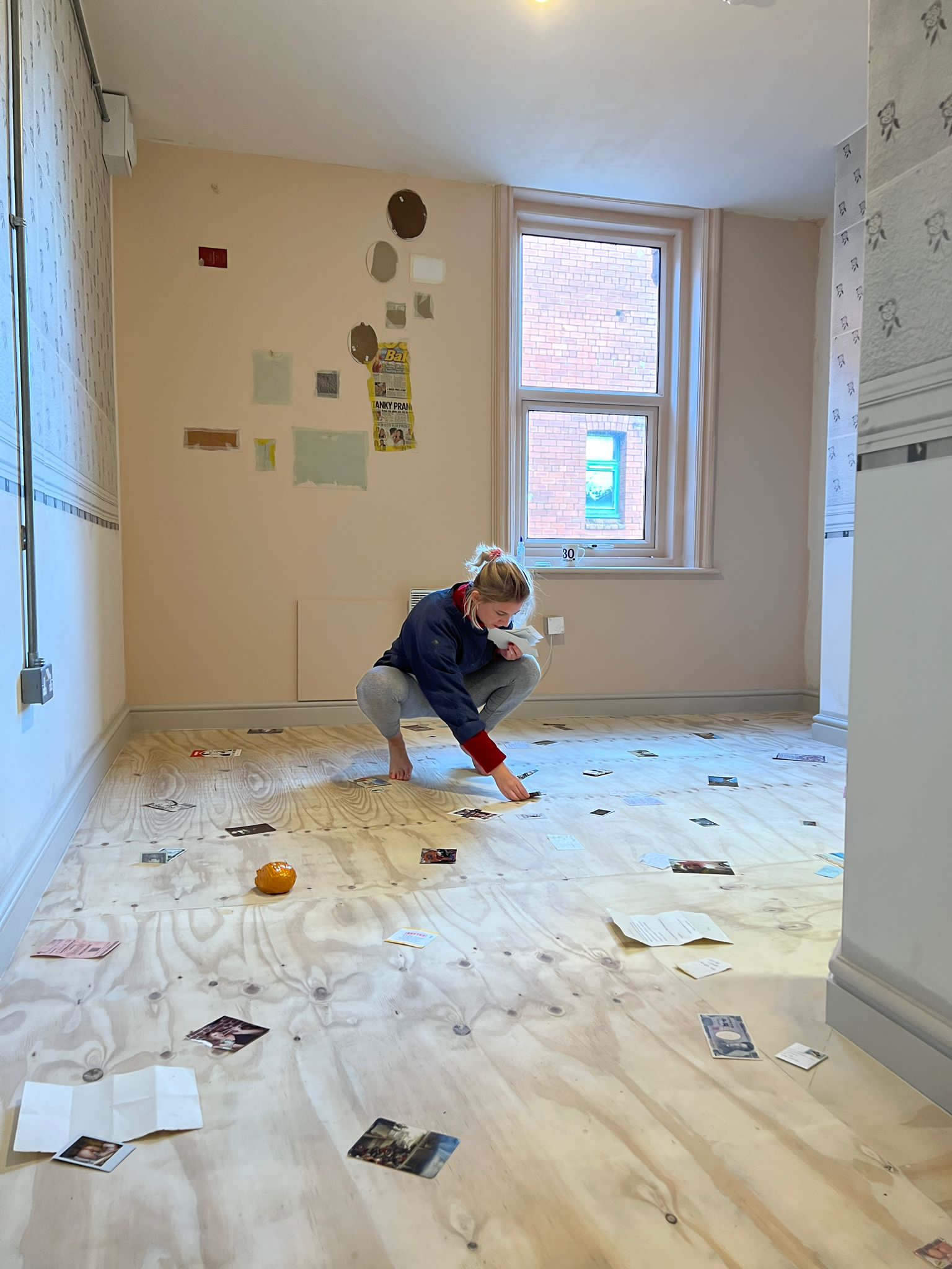 Emma creating the base layer of a floor for her commission at he Art Hostel. The wooden floor is covered in confetti, party poppers, photos, postcards, notes, ticket subs and other ephemera. Emma is knelt down adding more pieces.