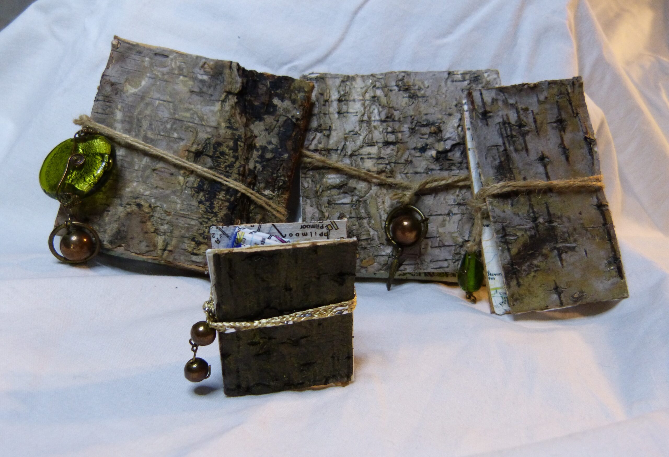 Four artist books with rough birch wood covers, secured with hessian string which has beads attached to the ends