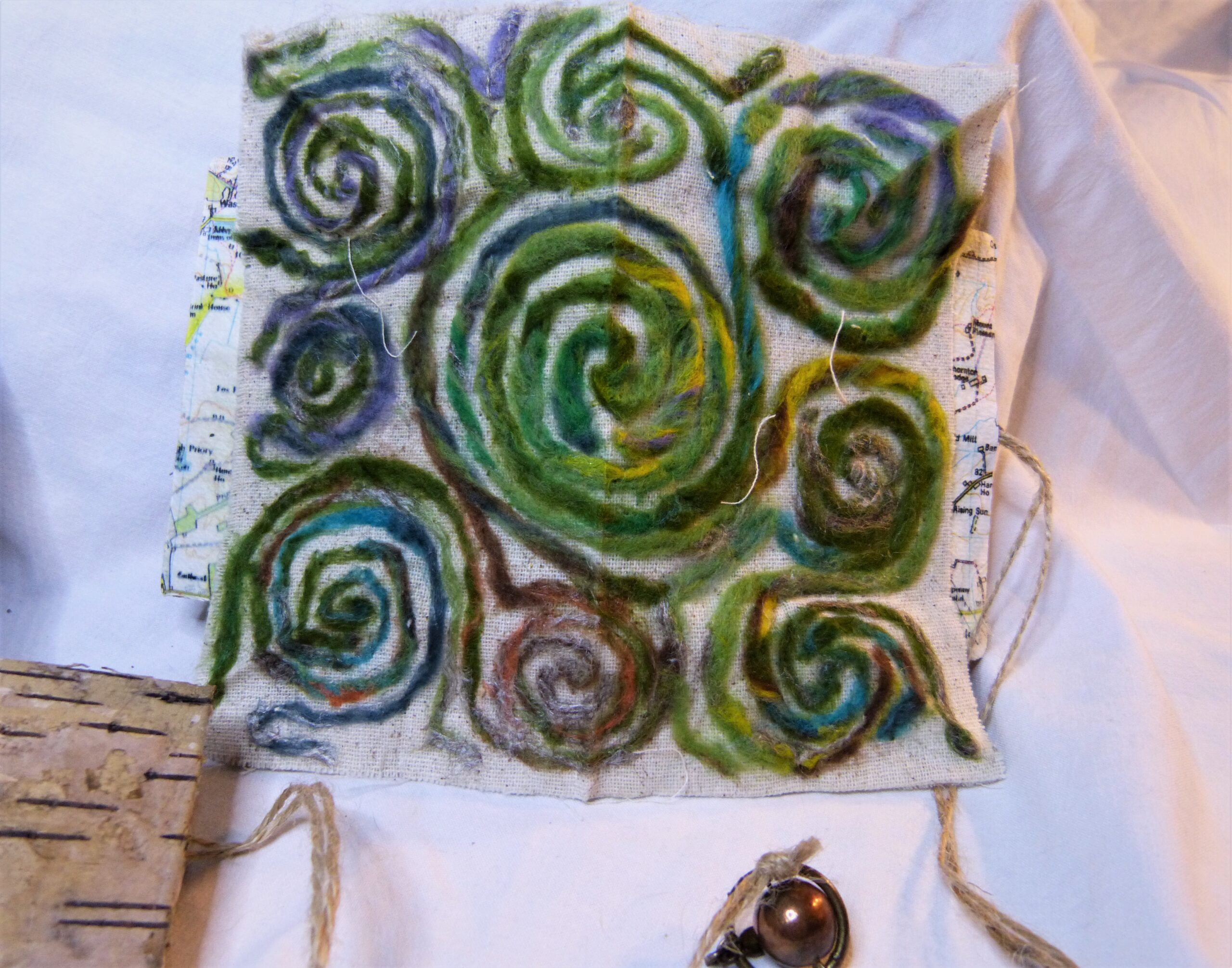 The interior of an artist book shows a circular maze created from twisted felting wool in shades of green and blue